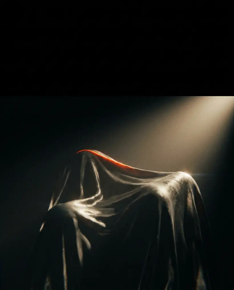 A monumental draped form raked by hard light against deep black, with a thin orange highlight along its peak.